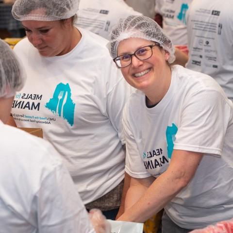 一名志愿者微笑着穿过人群，帮助为缅因州的食物活动打包食物包